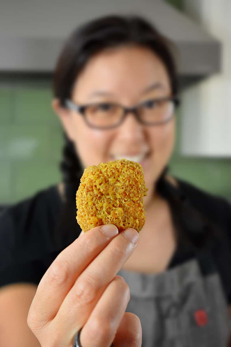A smiling Asian woman is holding up a golden air fryer chicken nugget.