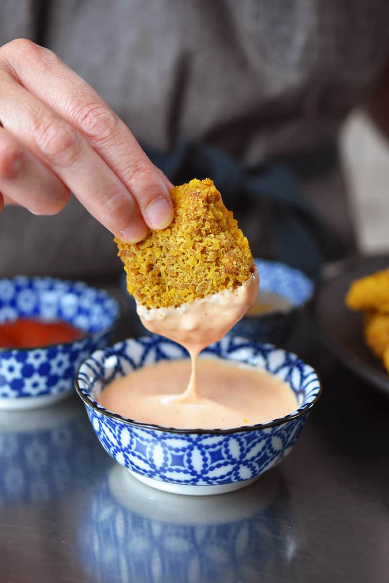 A hand is dipping a gluten-free air fryer chicken nugget into a bowl filled with sriracha mayonnaise.