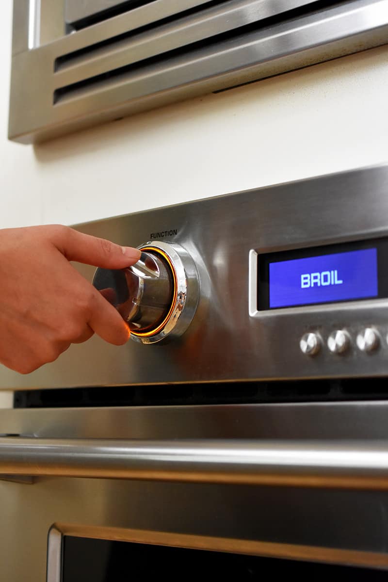 A hand is setting a wall oven to broil.