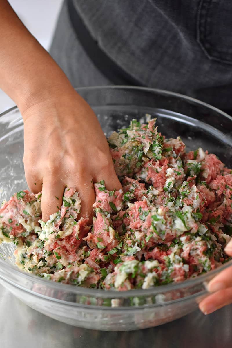 A hand is mixing Italian meatball mixture in a glass bowl.