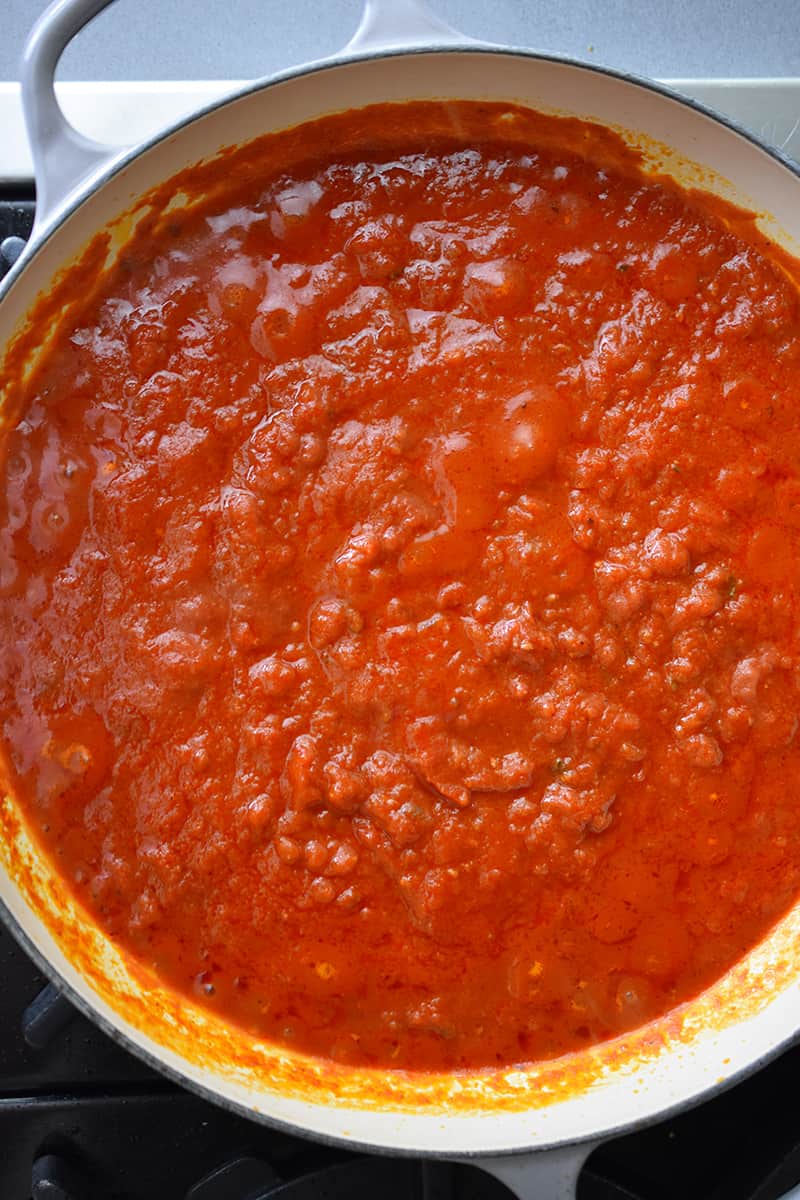 An overhead shot of a Le Creuset skillet filled with simmering marinara sauce.