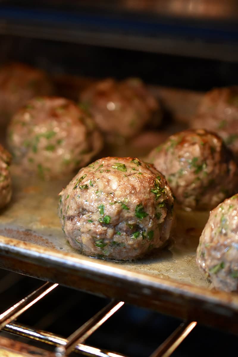 A closeup of Italian meatballs browning under a broiler in an oven.
