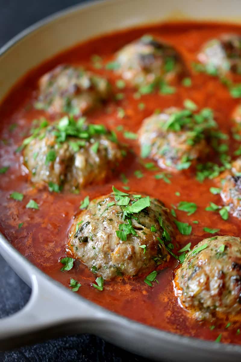 A side view of an enameled cast iron skillet filled with Italian meatballs and tomato sauce 