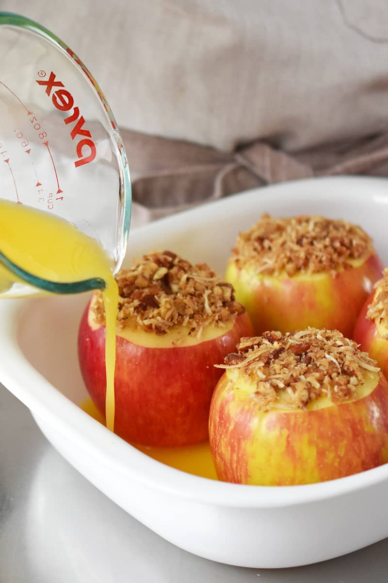 Pouring orange juice from a Pyrex measuring cup into a baking dish filled with stuffed apples