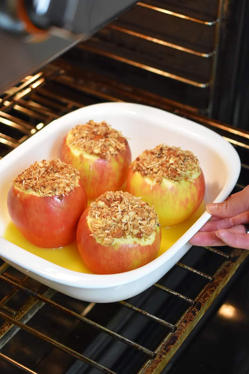A baking dish with baked apples is put into an open oven.