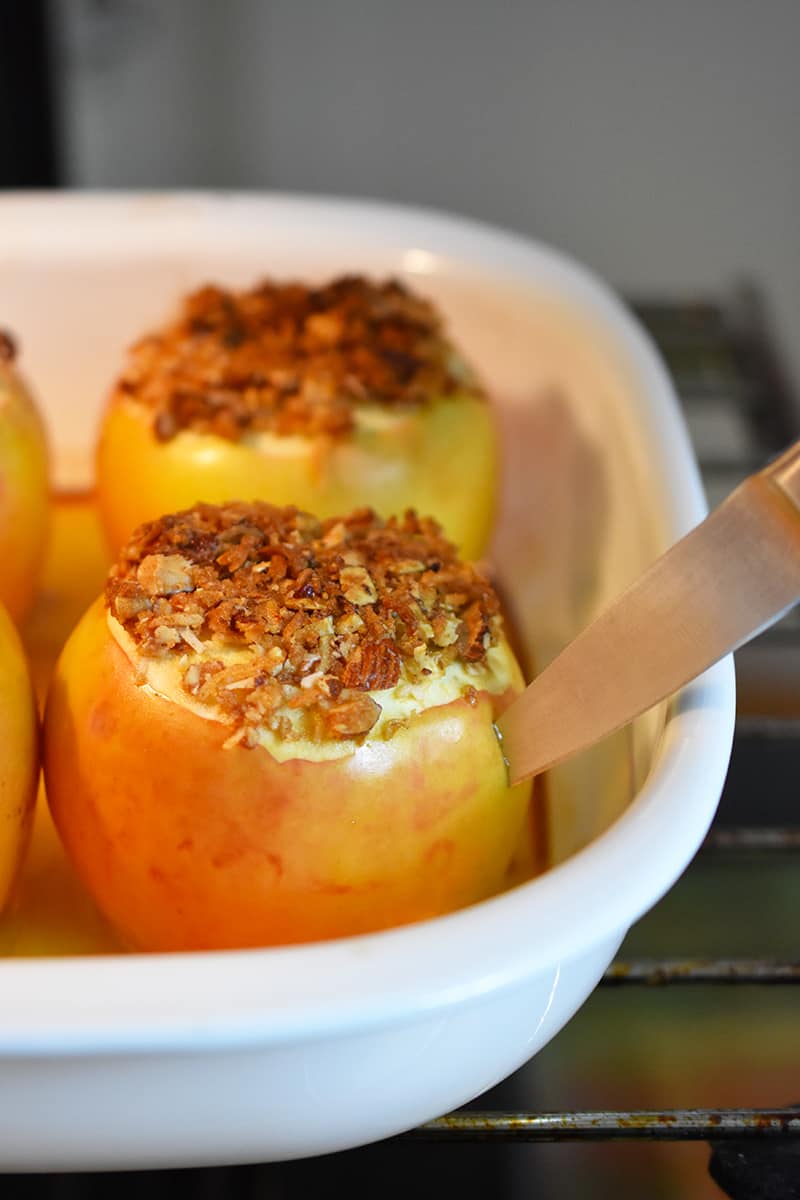A paring knife is inserted into a baked apple in an open oven.
