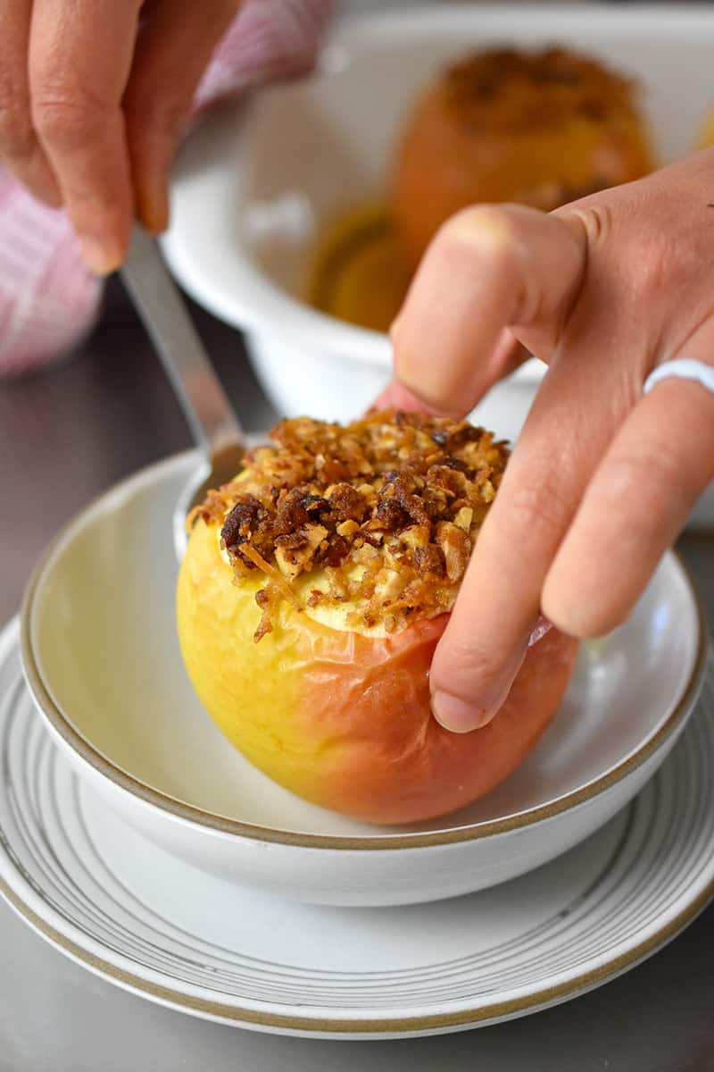 A hand is placing a baked apple in a shallow bowl.