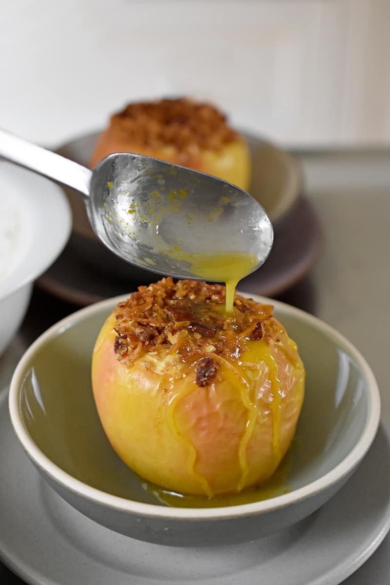 A spoon is pouring the concentrated orange juice onto a baked apple.