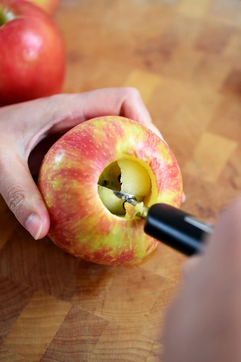 A melon baller is scooping out the stem and core of a Honeycrisp apple.