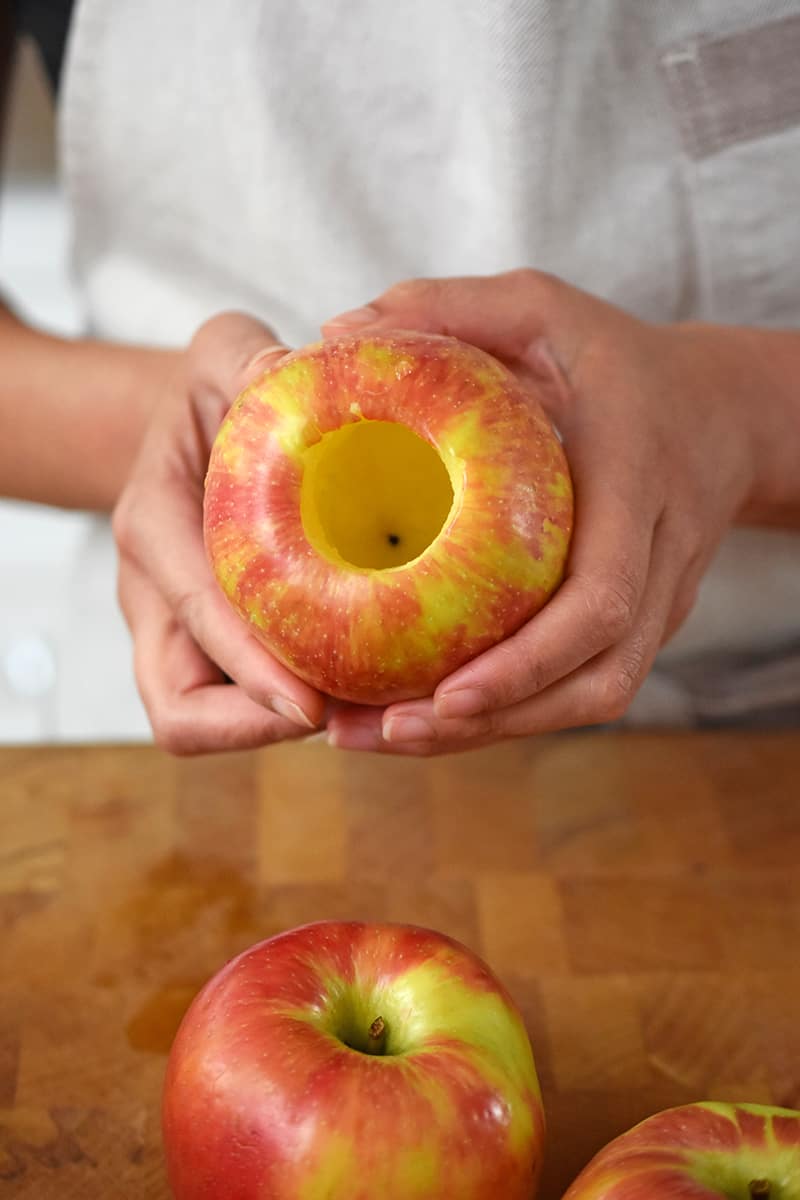 Two hands are holding an apple that has had the core and seeds removed.