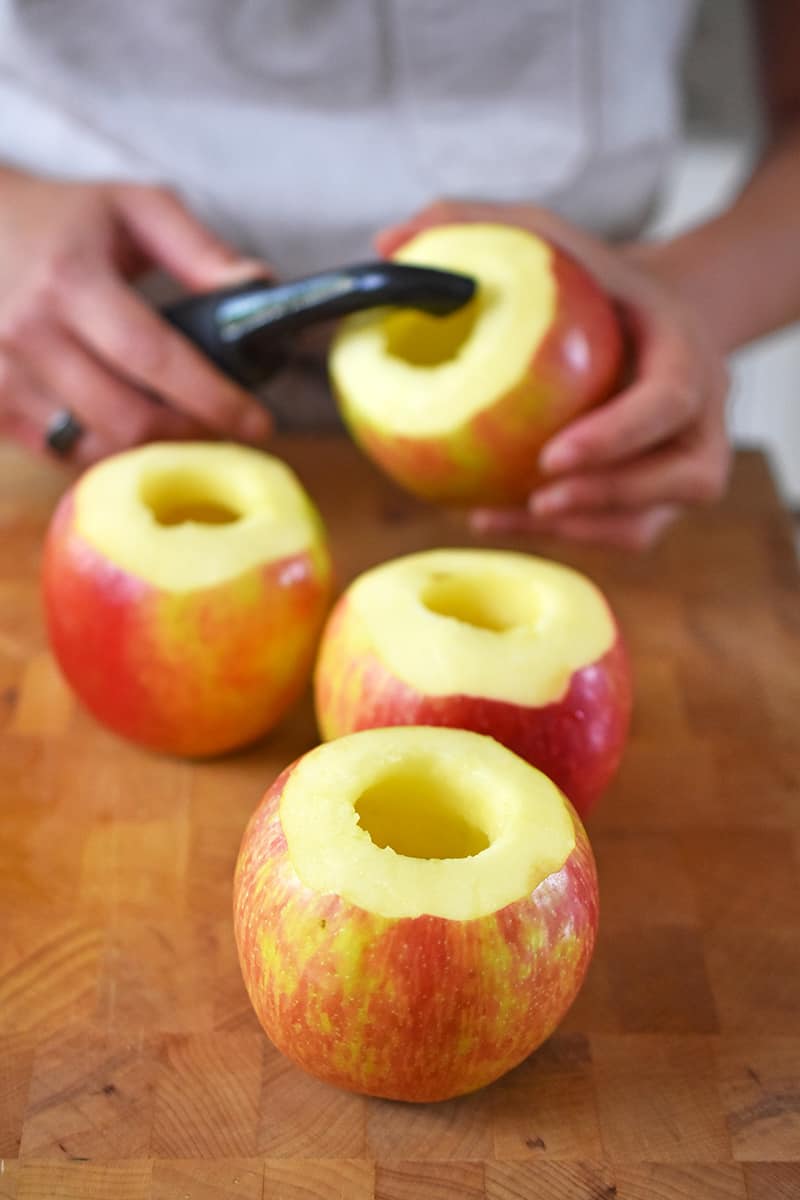 Four cored apples have the top peeled of their skin.