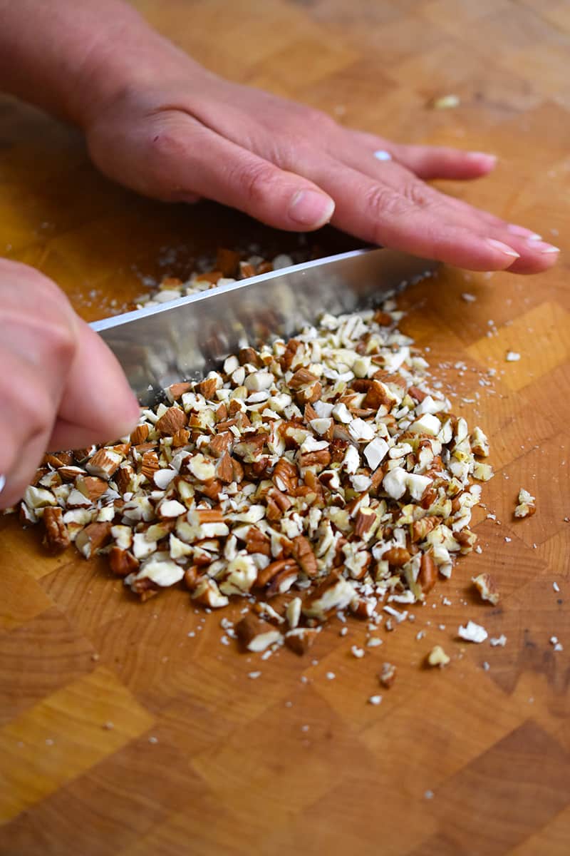 Cutting pecans and almonds with a chef's knife on a wooden cutting board