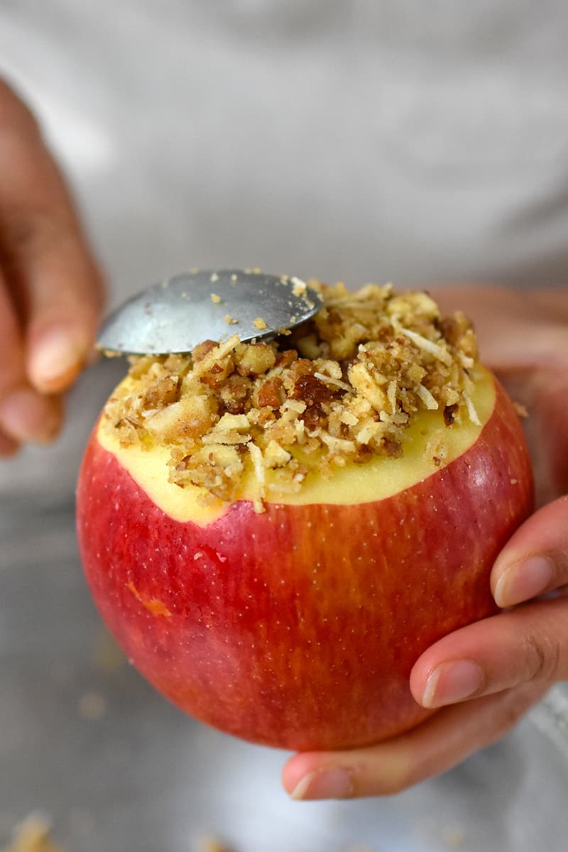A spoon is adding baked apple filling to the top of an apple, covering the unpeeled portion.