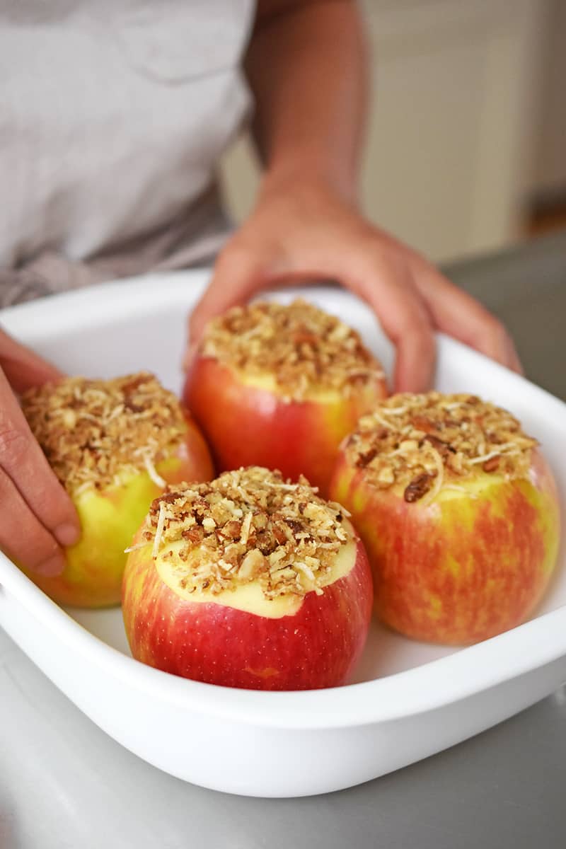Two hands are placing stuffed apples into a white baking dish.