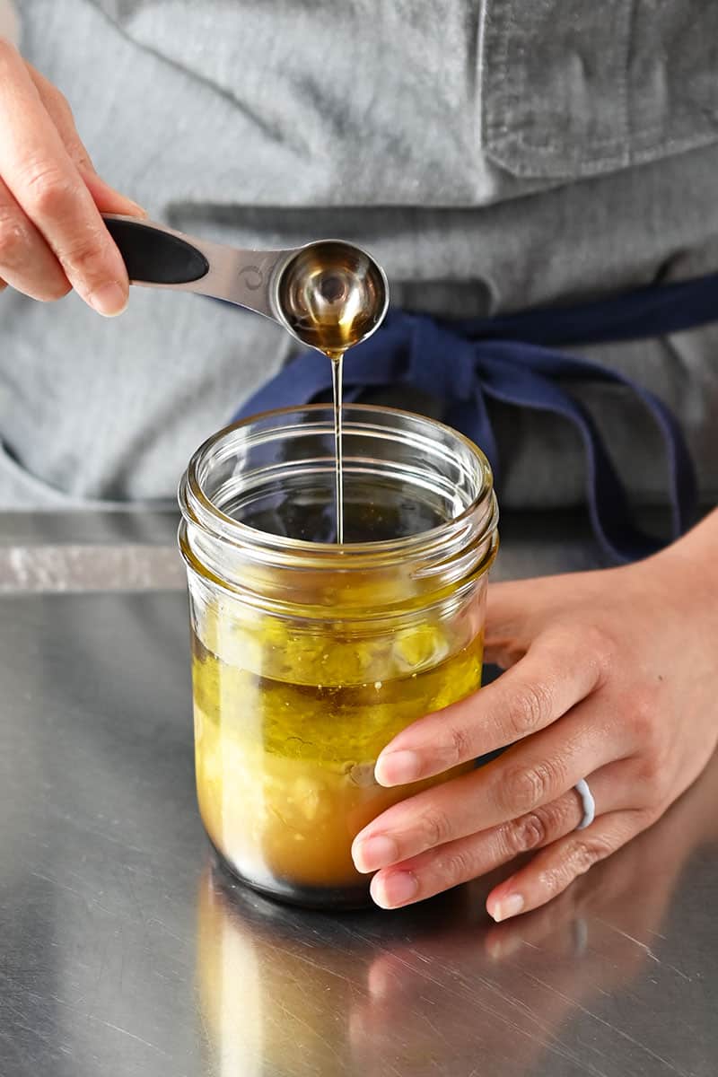 Adding a spoonful of toasted sesame oil to a mason jar filled with ingredients to make sesame ginger dressing