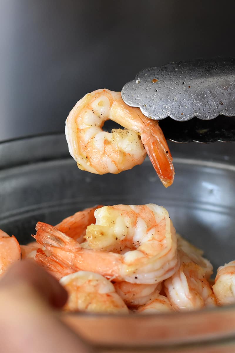A pair of tongs is holding up a perfectly cooked pan-fried shrimp.