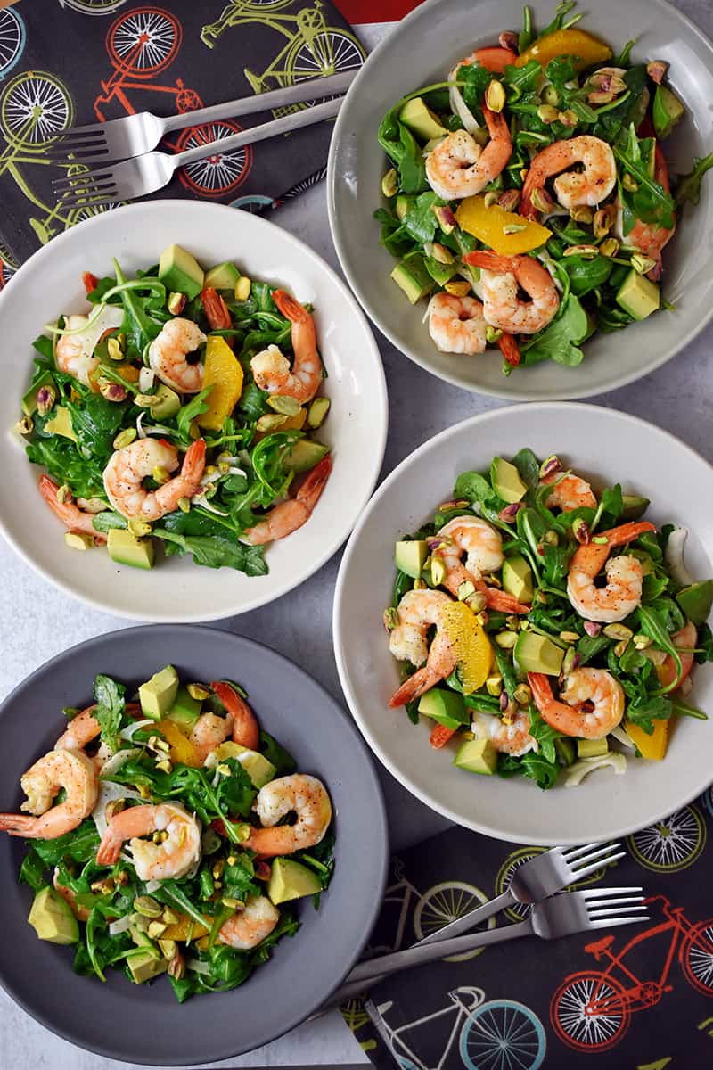 An overhead shot of four bowls of shrimp and avocado salad with fennel, arugula, orange segments, and pistachios.