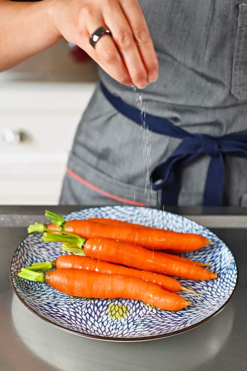 Sprinkling salt on some carrots on a blue and white plate.