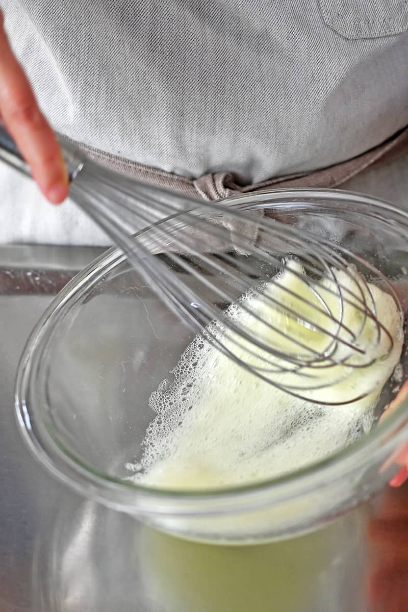 A whisk is beating egg whites until they are frothy in a glass bowl.
