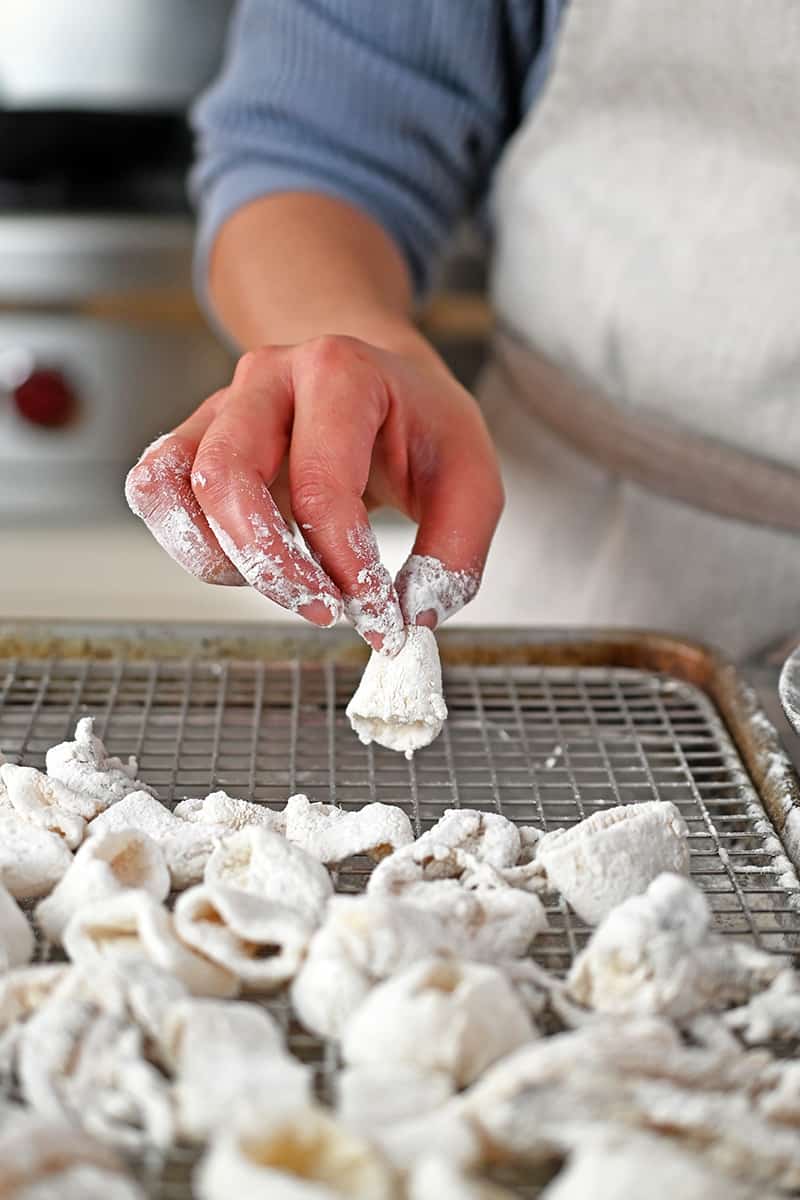 A hand is adding dredged calamari rings to a rack on a rimmed baking sheet.