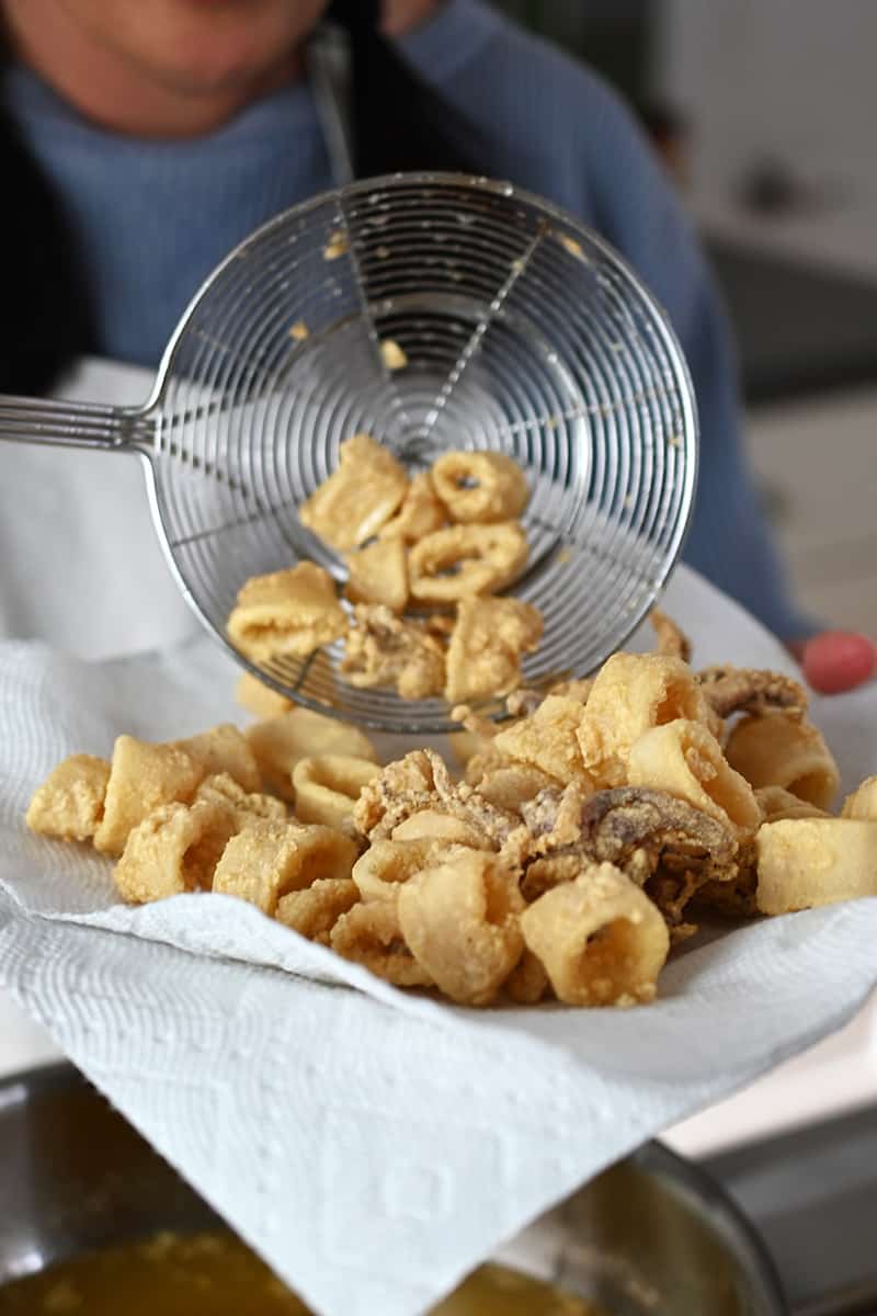 Transferring golden brown paleo fried calamari with a strainer to a paper-towel lined plate.
