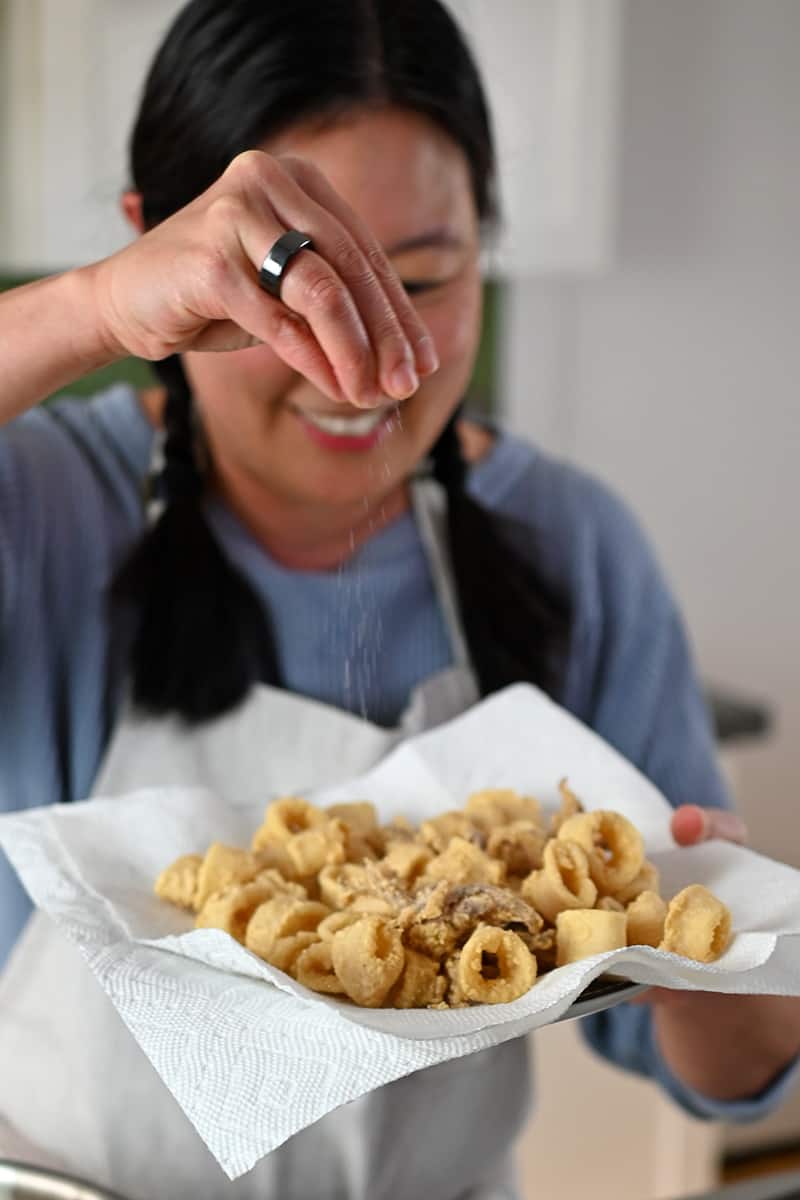 A smiling Asian woman is sprinkling salt to a plate of fried calamari.