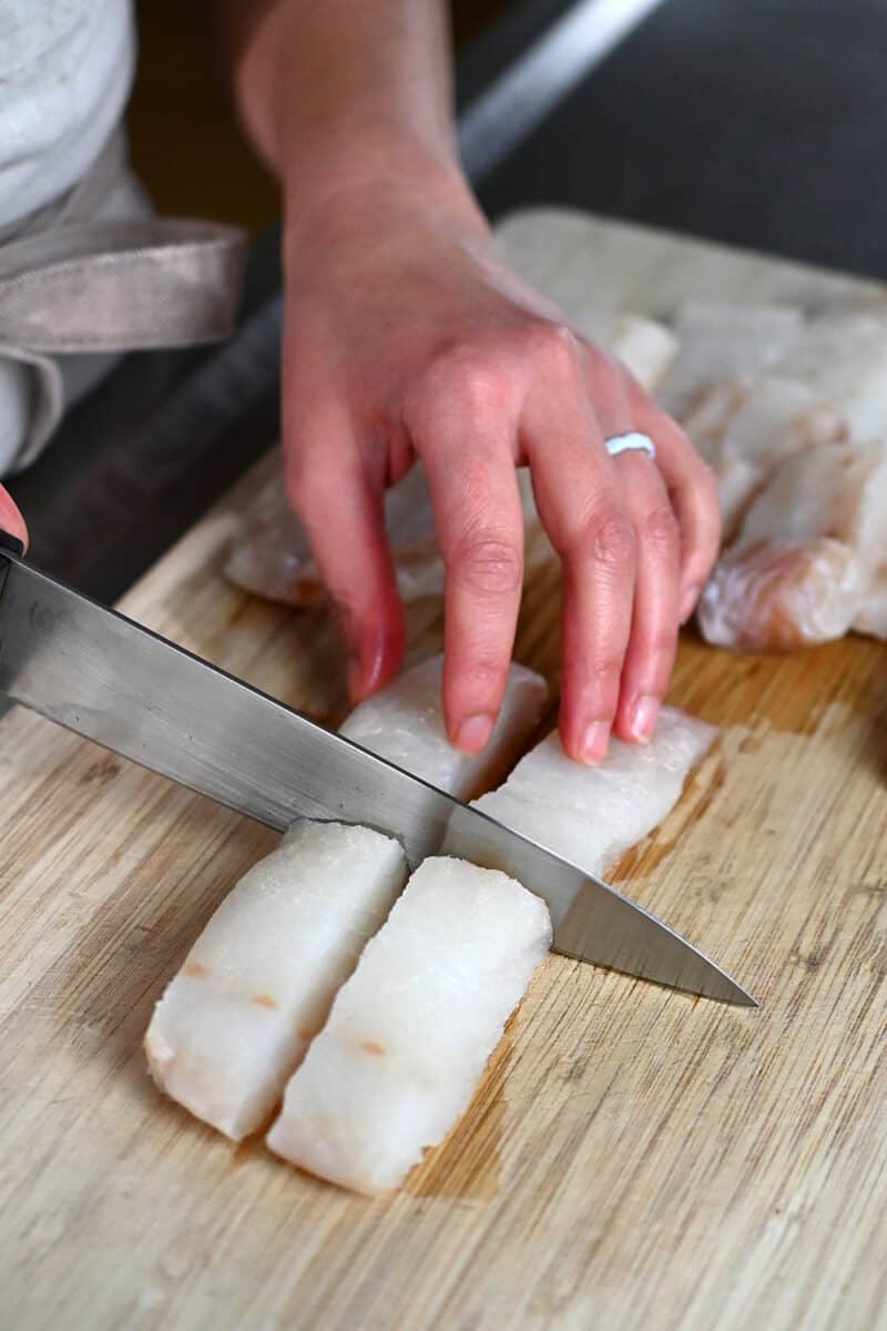 A boneless and skinless cod fillet is being cut into four uniform pieces.