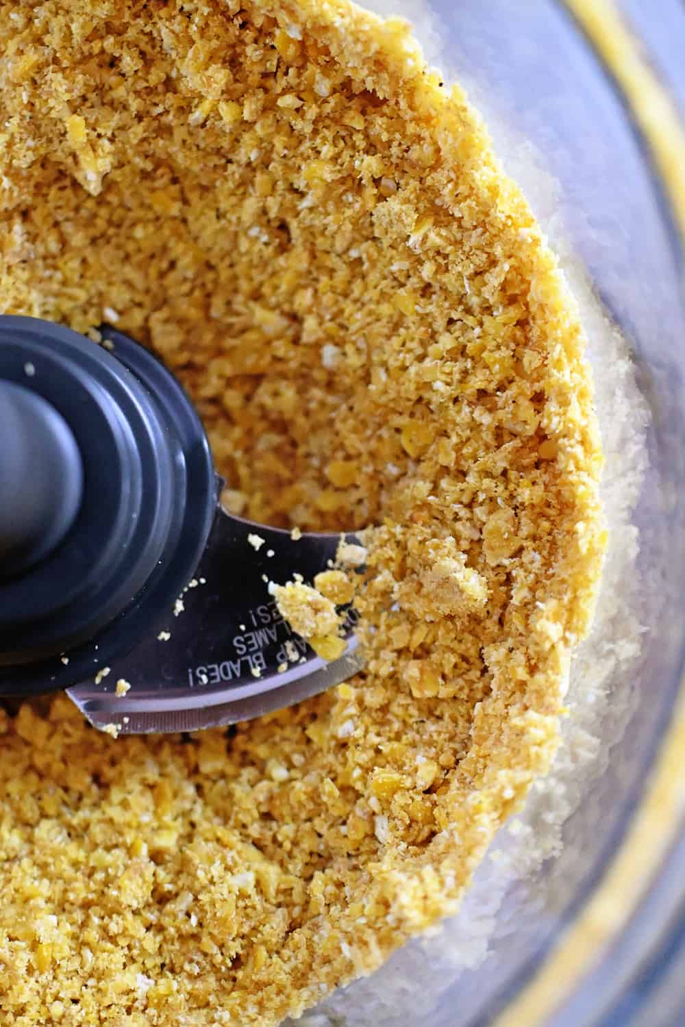 An overhead shot of plantain chip crumbs in an open food processor