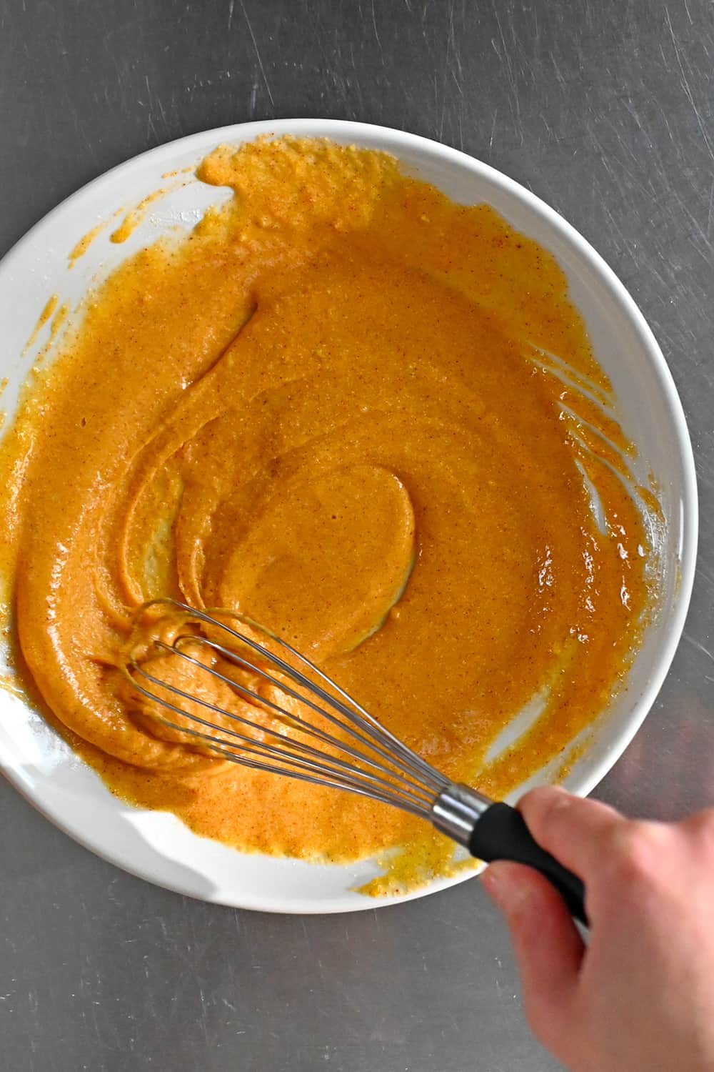 An overhead shot of a whisk combining the egg, flour, and spice batter for the paleo fish sticks