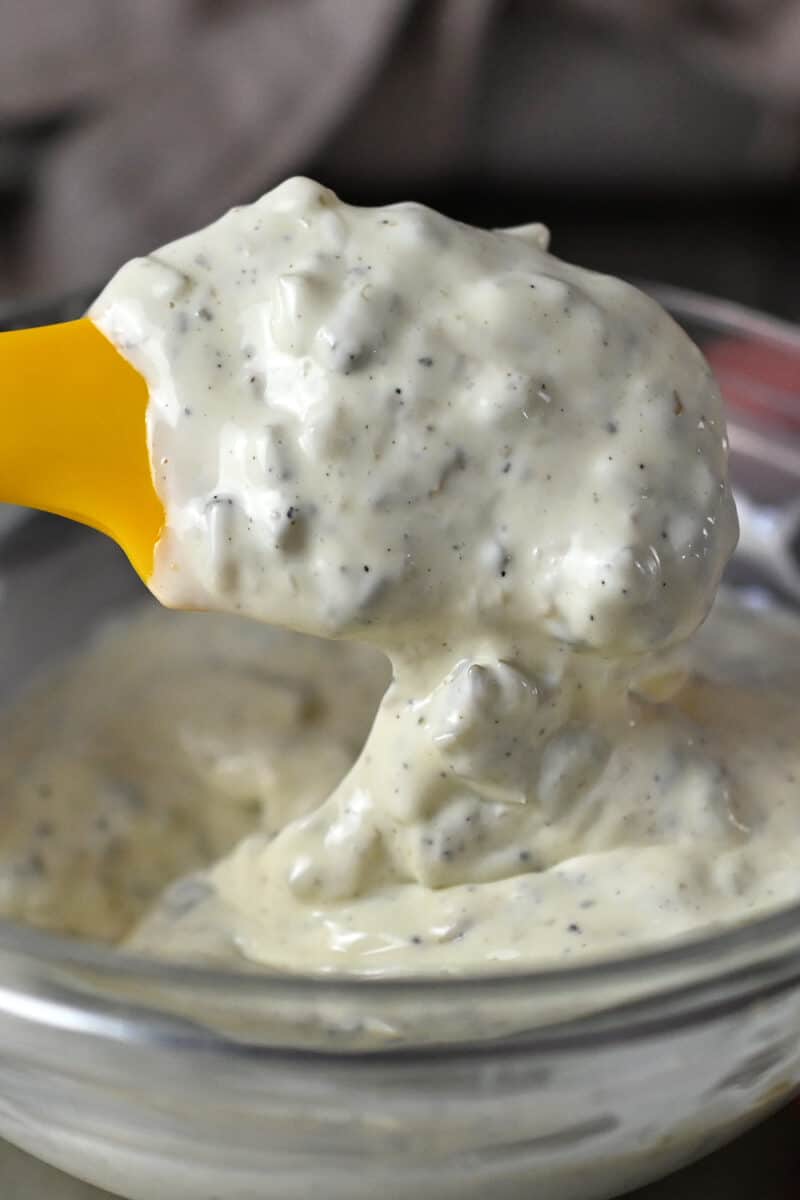 A yellow spatula is mixing tartar sauce in a glass bowl.