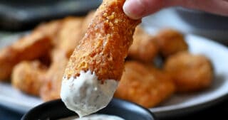 A hand is dipping a fish stick in tartar sauce