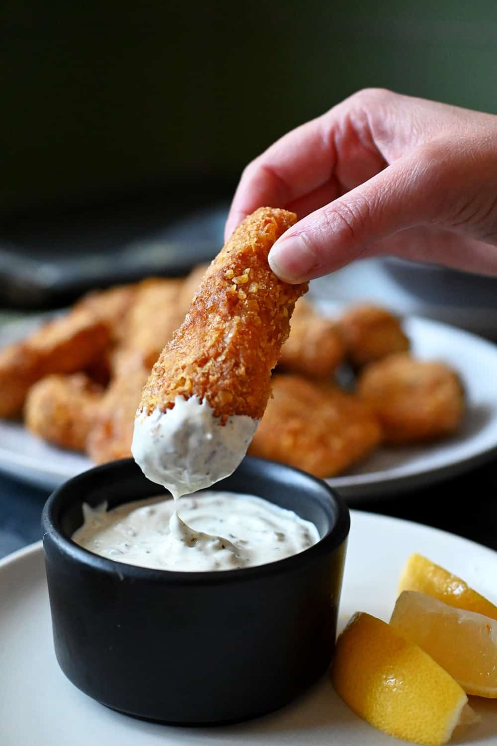 A hand is dipping a fish stick in tartar sauce
