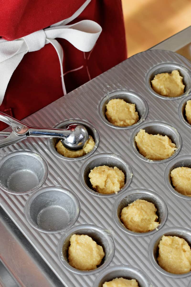 Adding a small scoop of financiers batter to a greased mini muffin pan