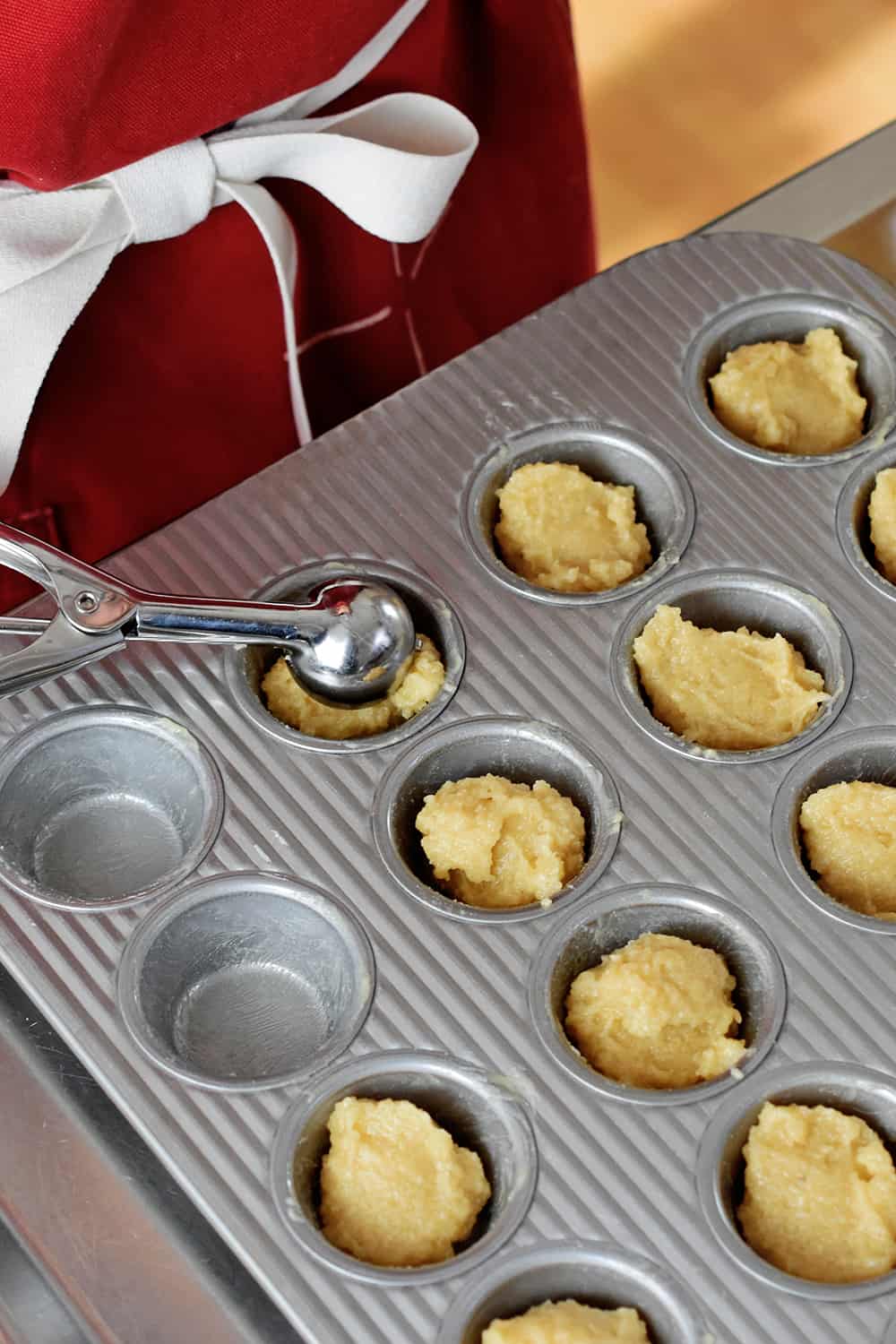 Adding a small scoop of financiers batter to a greased mini muffin pan