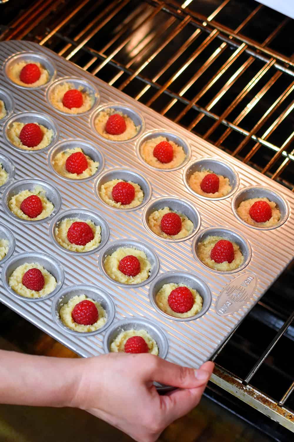 A mini muffin pan of raspberry financiers is being put into a hot oven