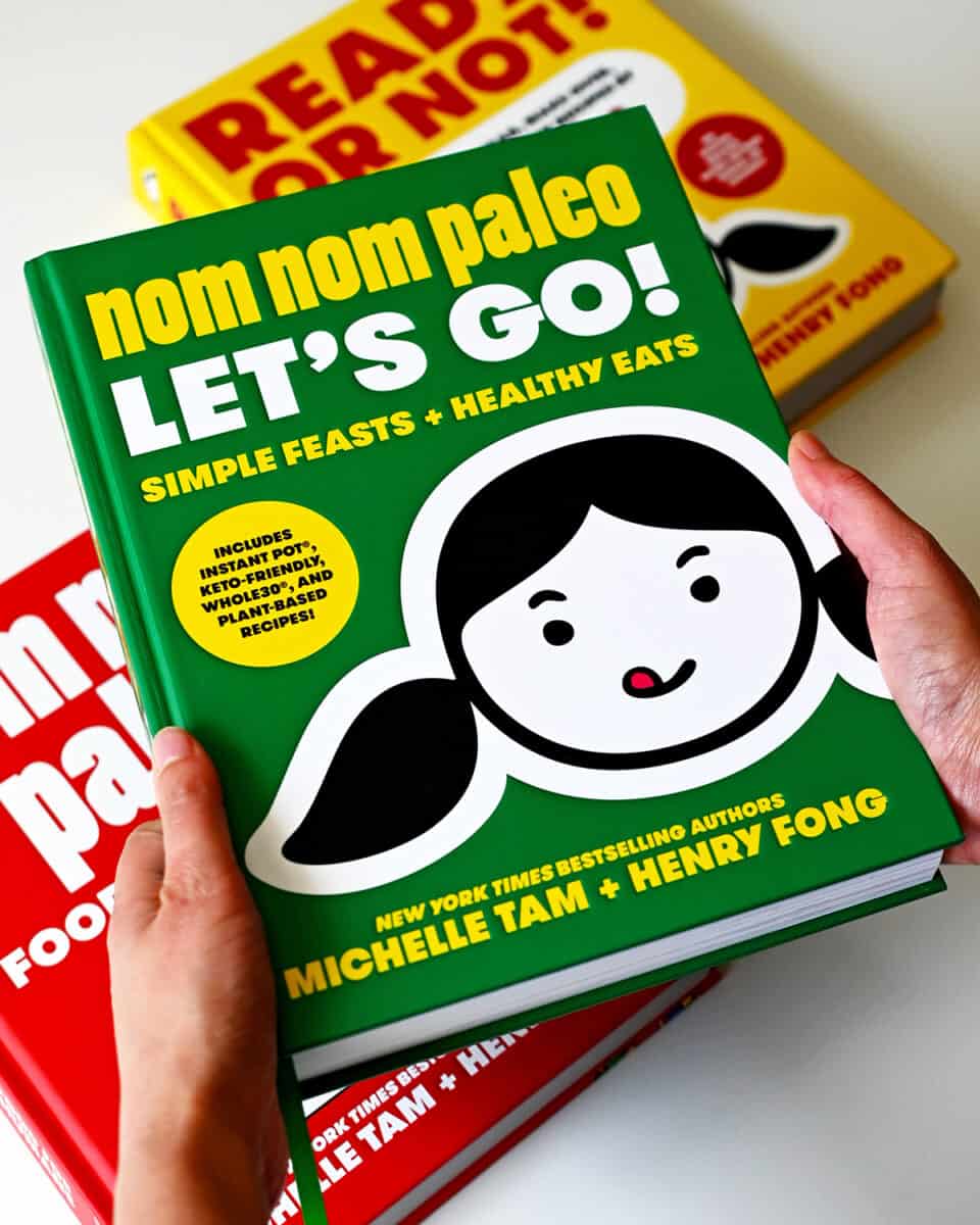 Two hands holding a copy of the Nom Nom Paleo: Let's Go! cookbook by Michelle Tam and Henry Fong
