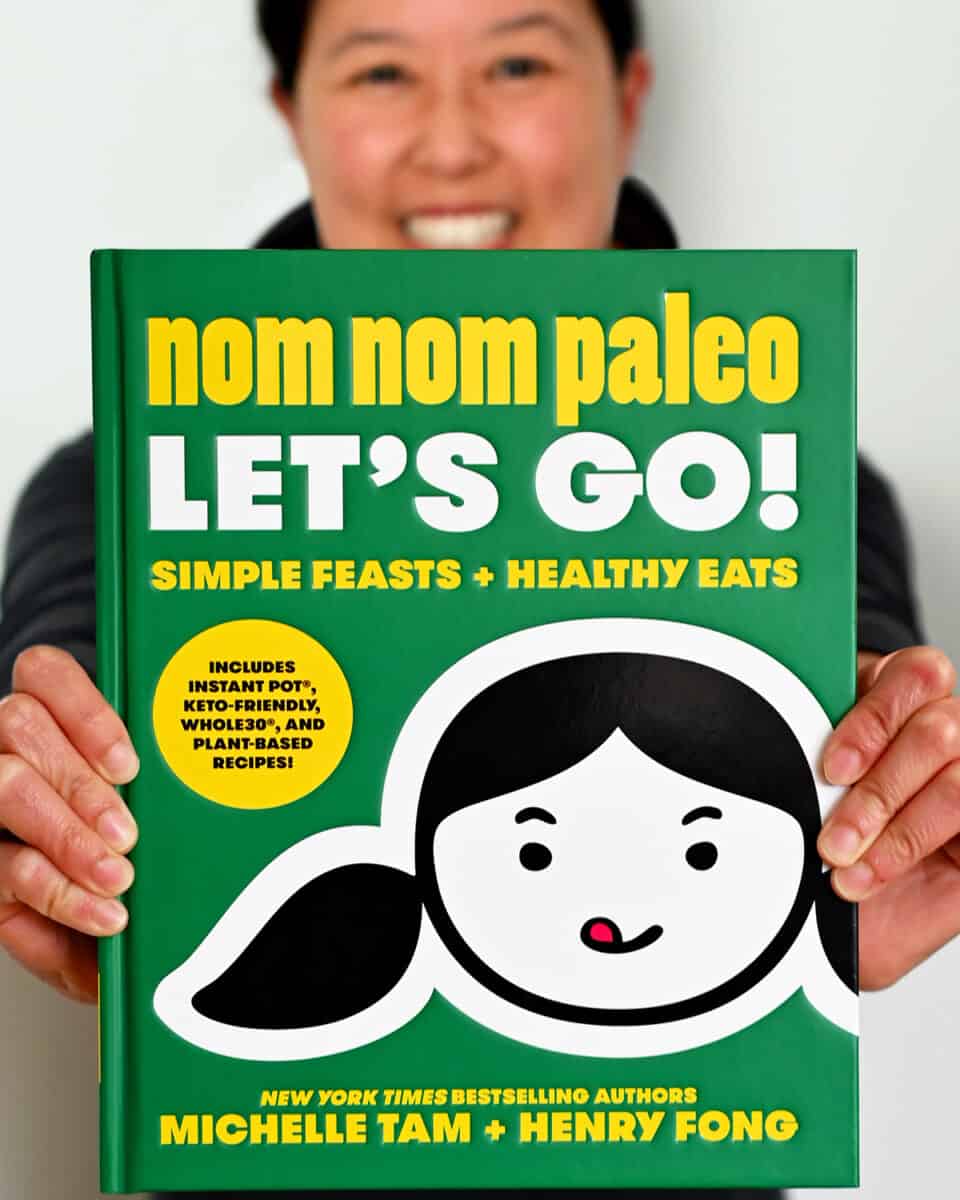 Two hands holding out a copy of the Nom Nom Paleo: Let's Go! cookbook by Michelle Tam and Henry Fong