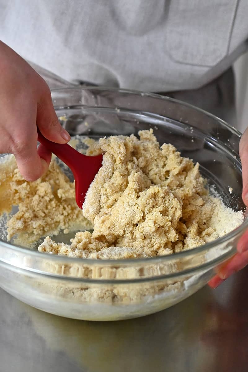 Combining the wet and dry cookie dough ingredients in a glass bowl with a red spatula
