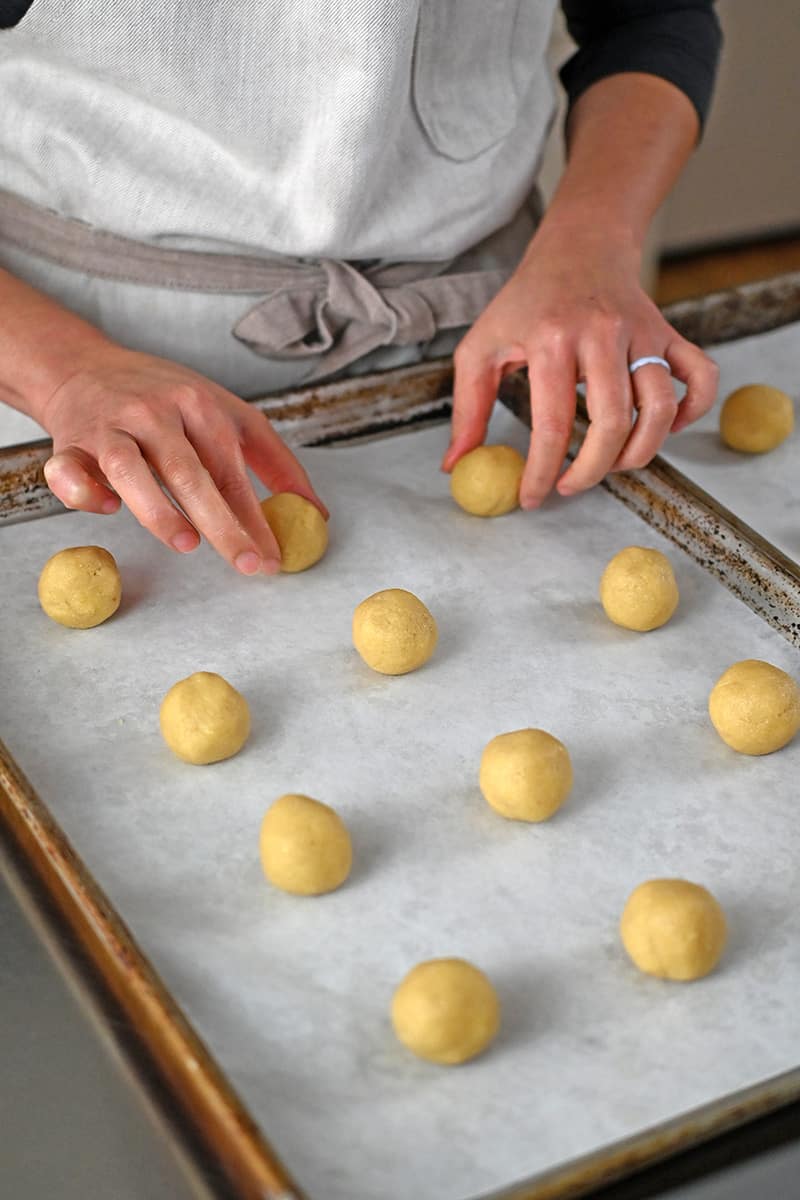 Two hands are arranging balls of cookie dough on a parchment lined rimmed baking sheet.