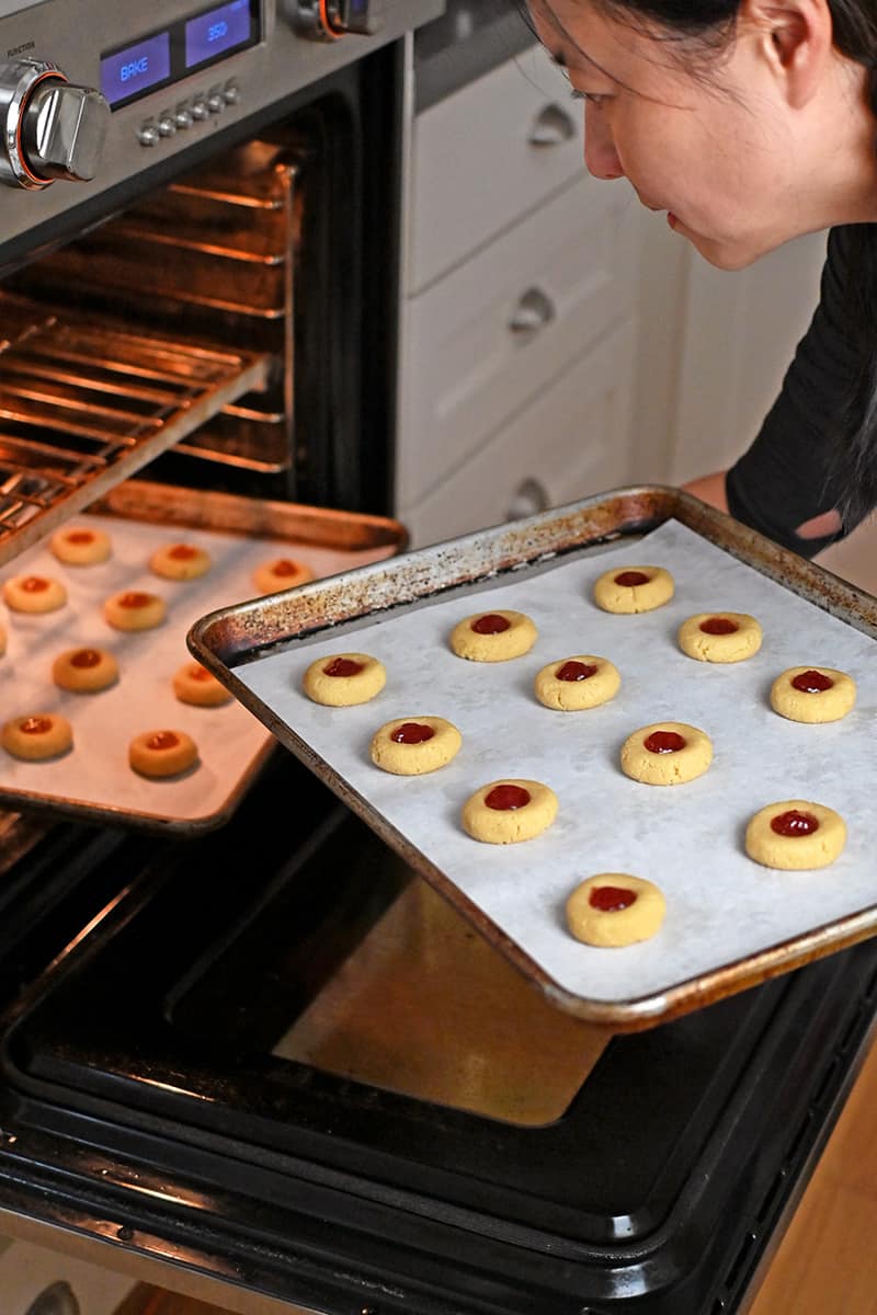 An Asian woman is removing paleo thumbprint cookies from the oven.