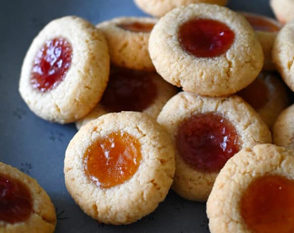 A blue plate is piled with paleo and gluten free thumbprint cookies filled with apricot and strawberry jam.