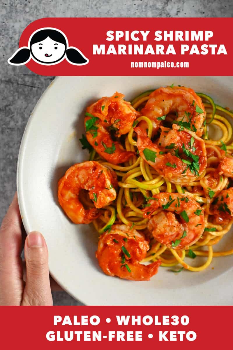An overhead shot of a hand holding a bowl filled with Whole30 and keto spicy shrimp pasta with marinara sauce on zucchini noodles.