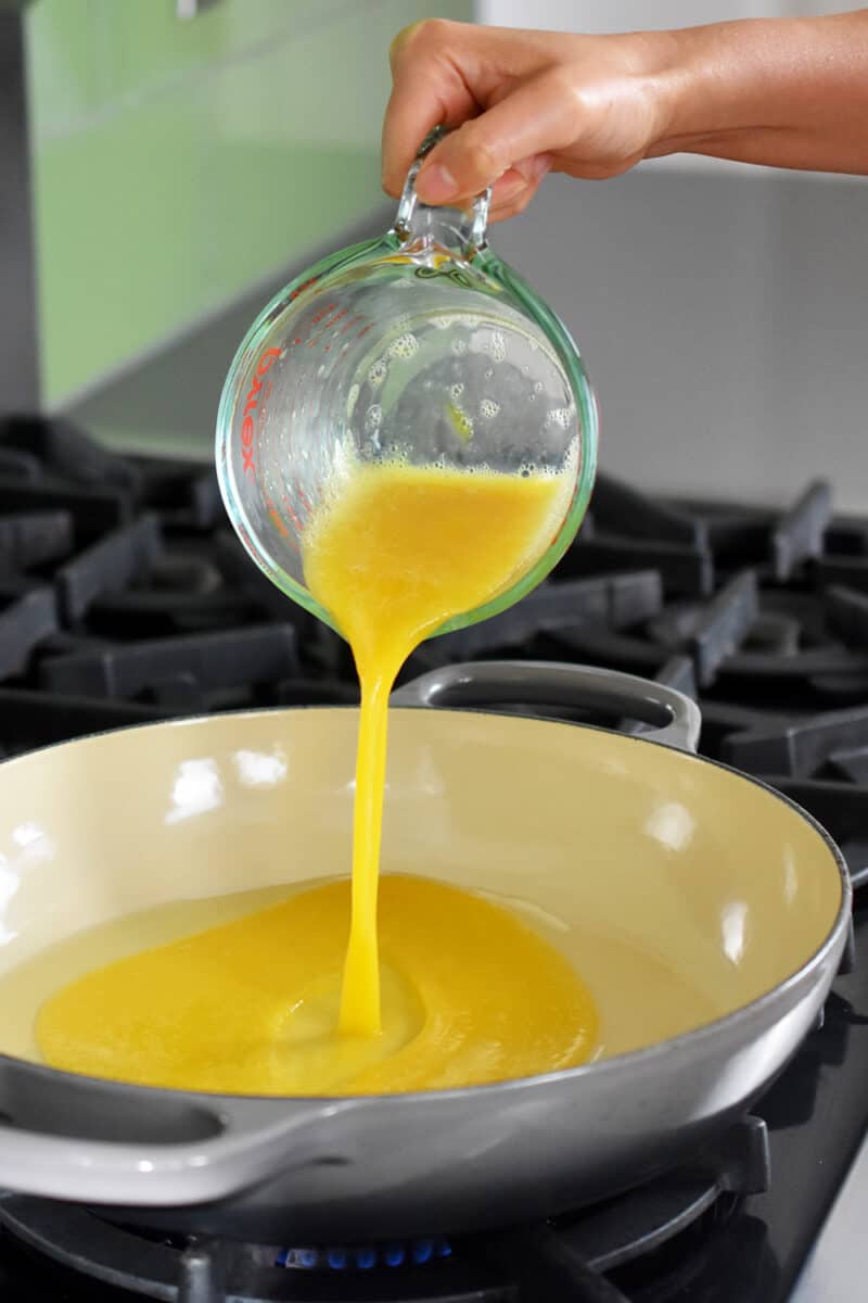 Pouring whisked eggs from a liquid measuring cup into a hot skillet 