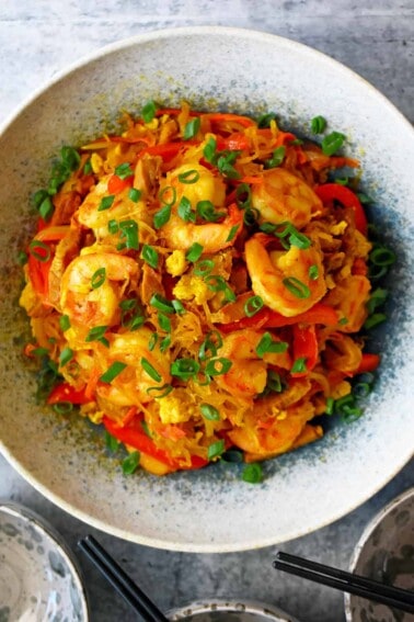 An overhead shot of a bowl of paleo and Whole30 Singapore noodles, topped with shrimp and sliced scallions.
