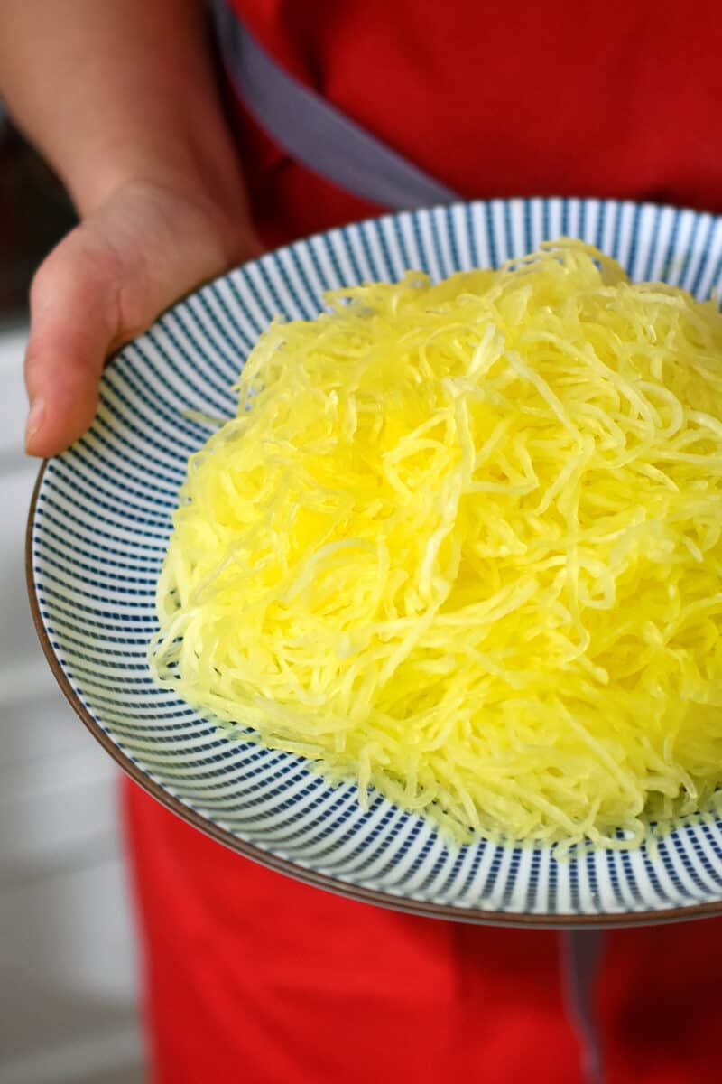A hand is holding a blue plate with cooked and shredded spaghetti squash