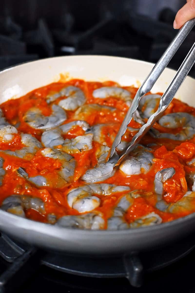 Adding large peeled shrimp into a skillet with spicy marinara sauce.