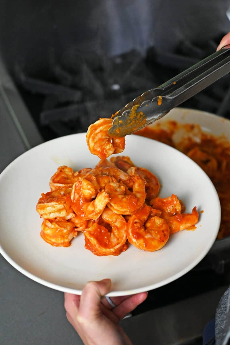 Using tongs to transfer cooked spicy shrimp to a platter.