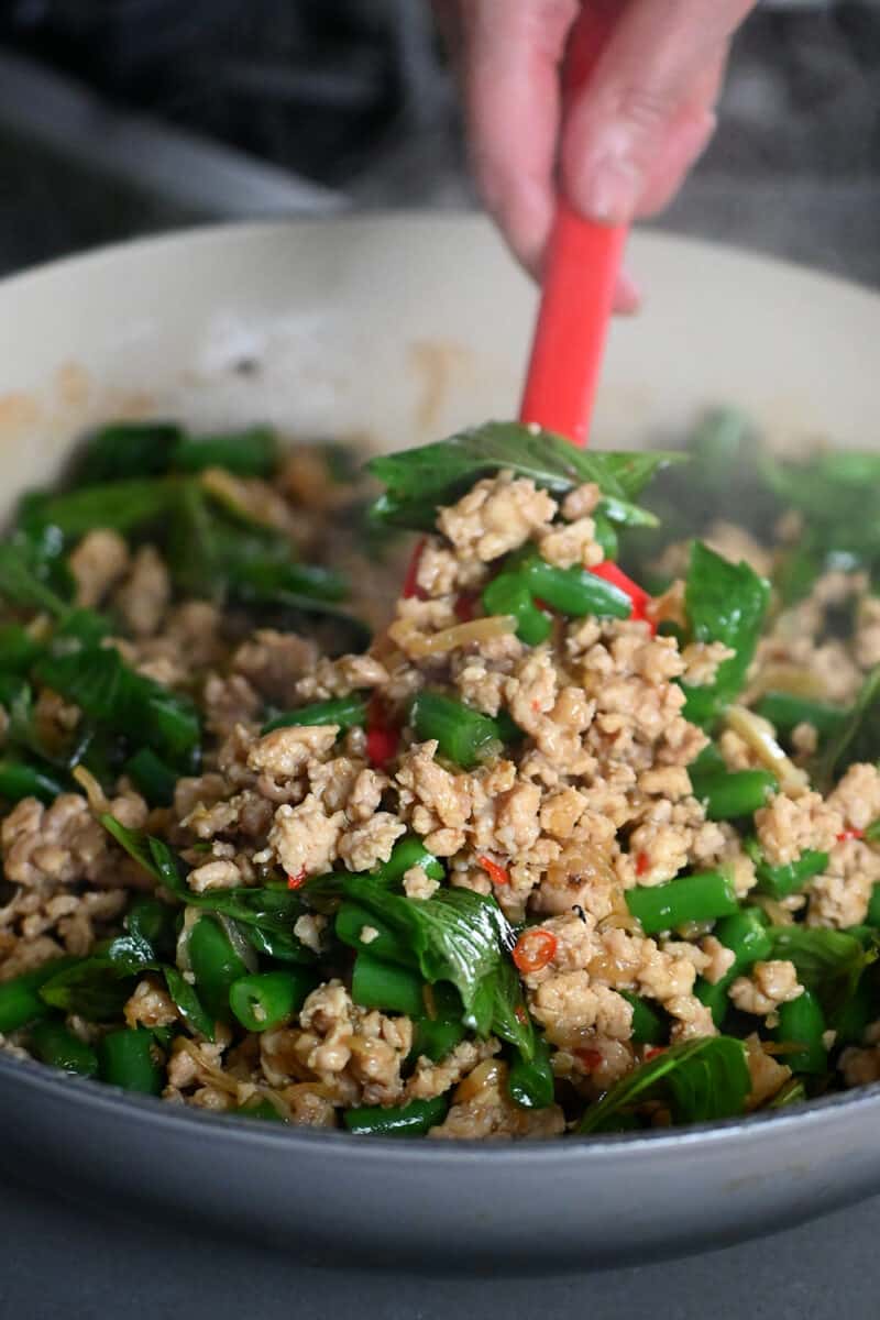 A red spatula is scooping up Thai Basil chicken from a skillet