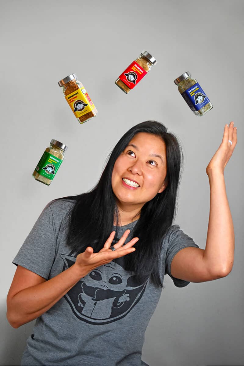 Photograph of a woman (Michelle Tam) juggling bottles of the new Nom Nom Paleo spice blends