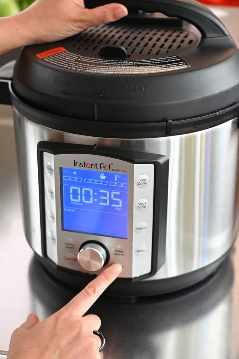 A finger is pressing a button on an Instant Pot that is set for 35 minutes under high pressure.